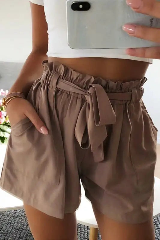Close-up view of women's high-waisted brown paperbag shorts with an adjustable tie belt and side pockets.