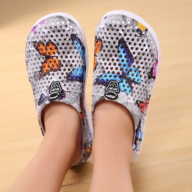 A pair of women's white clogs featuring a colorful butterfly pattern and a breathable hollow-out design, perfect for summer beach wear.