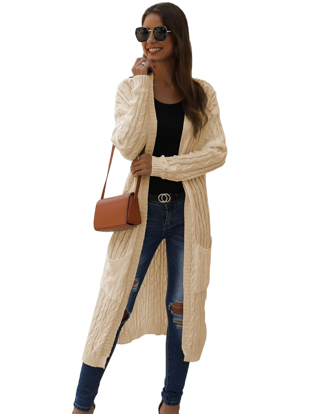 Model wearing a beige long sleeve open front cable knit cardigan with pockets over a black top and blue jeans.