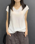 A woman wearing a V-neck short sleeve knit top in white, with a relaxed fit and simple button detail.
