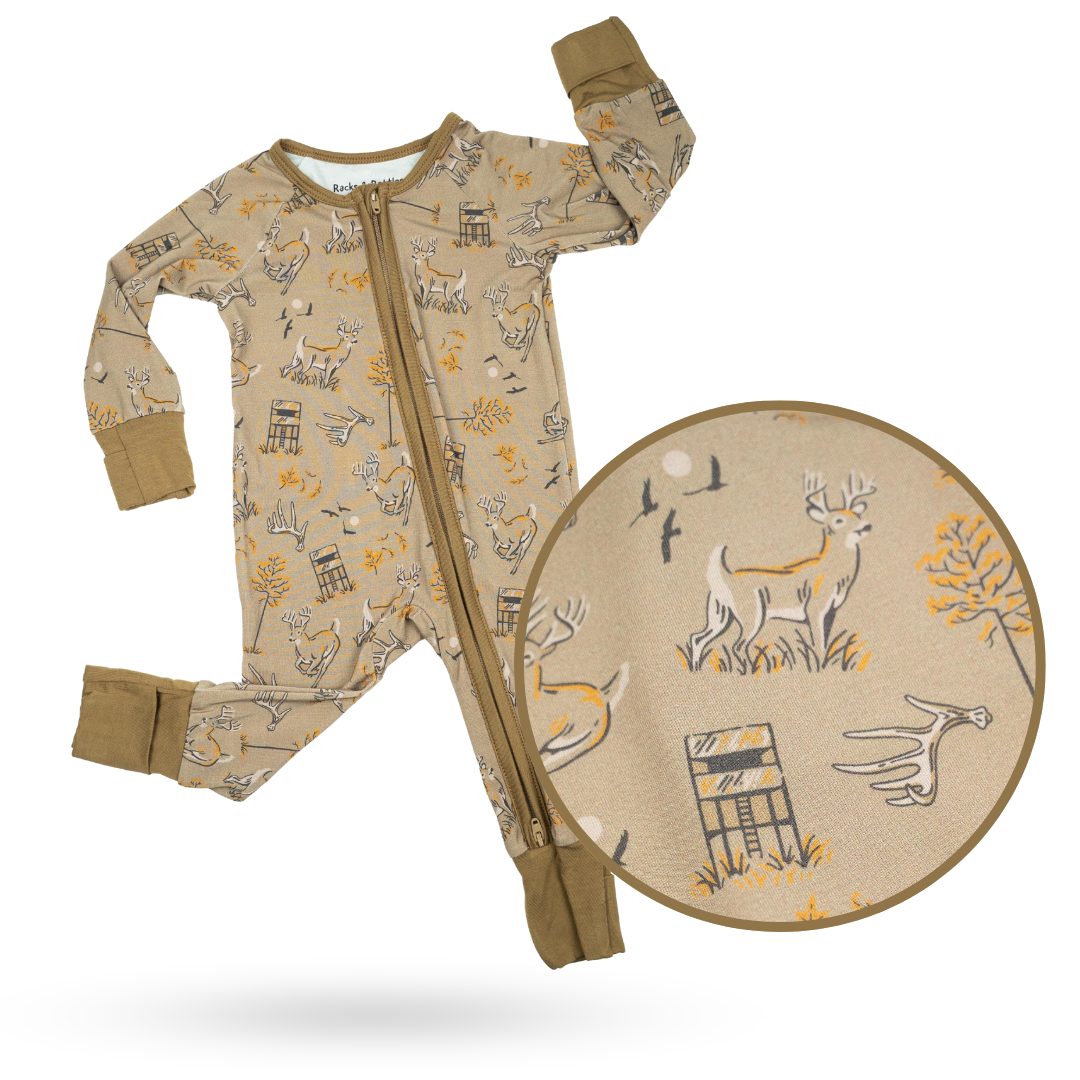 Baby wearing an Antler Club bamboo zippy in tan with a brown and mustard yellow deer forest pattern.