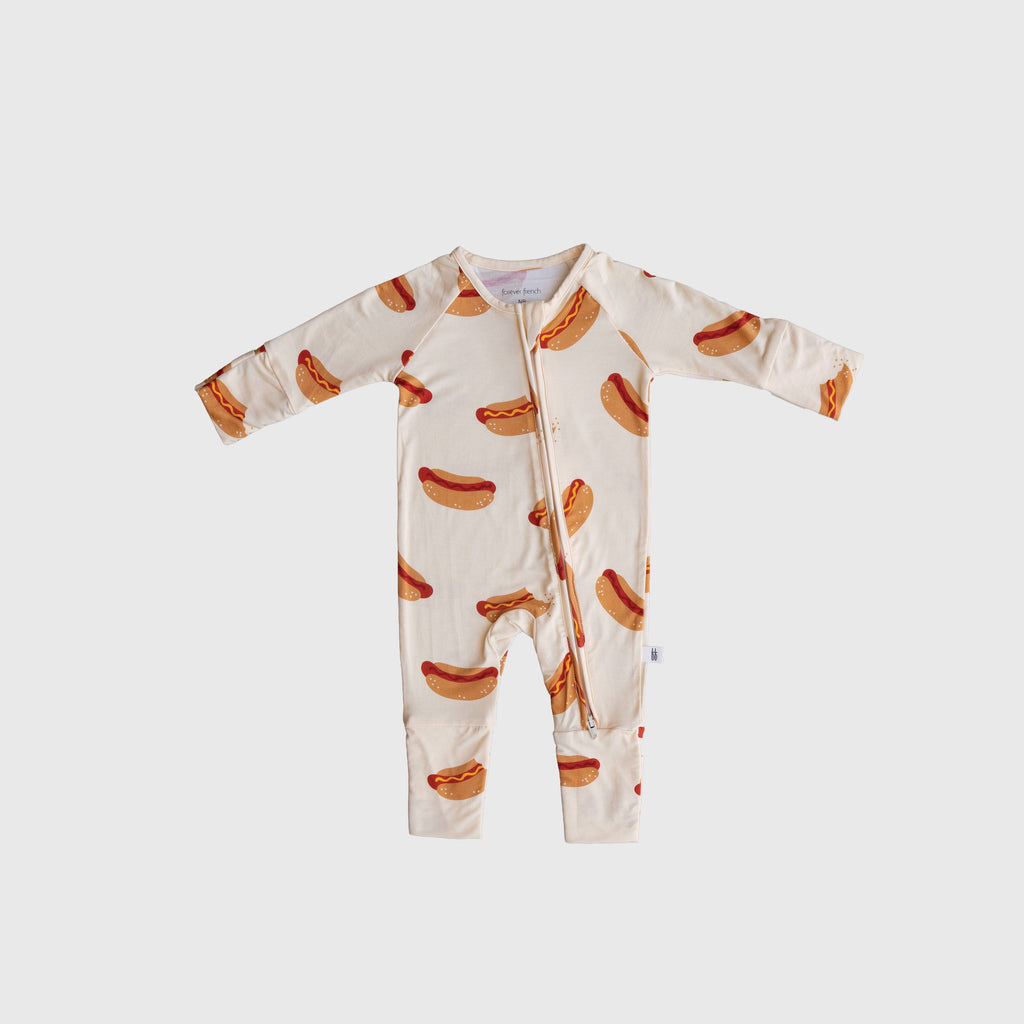 Baby wearing cream bamboo zip pajamas with whimsical hot dog pattern and rollover cuffs