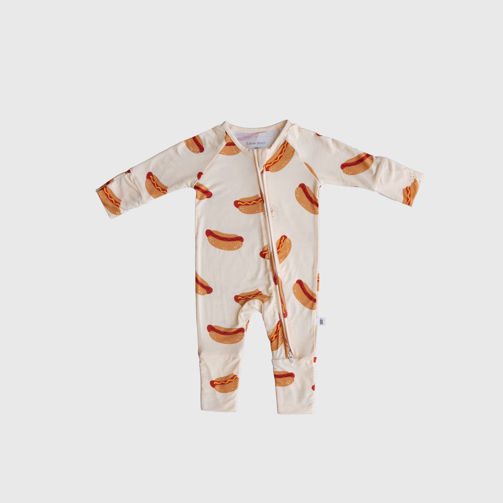 Baby wearing cream bamboo zip pajamas with whimsical hot dog pattern and rollover cuffs