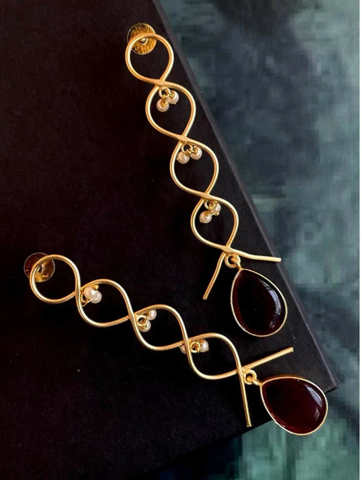 Close up of elegant cherry red Monalisa stone zigzag gold earrings on a display background