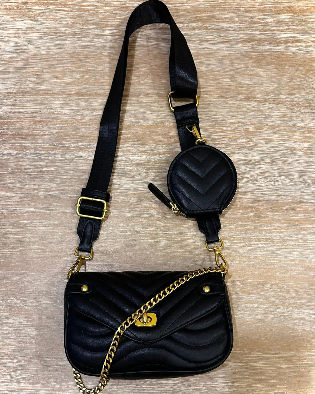 Black quilted handbag with gold chain and matching small round pouch on a wooden surface