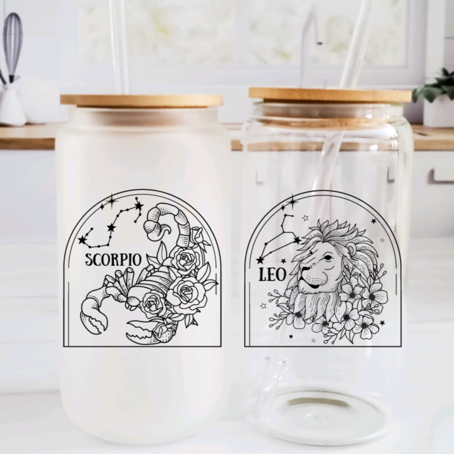 A 16oz glass can cup featuring a black zodiac constellation and floral design, shown with a bamboo lid and glass straw.