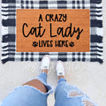 A Crazy Cat Lady Lives Here doormat featuring natural coir and a black and white buffalo plaid border on a porch.