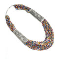 A long statement necklace featuring multi-colored beads and matte oxidized silver metal plates for a bohemian look.