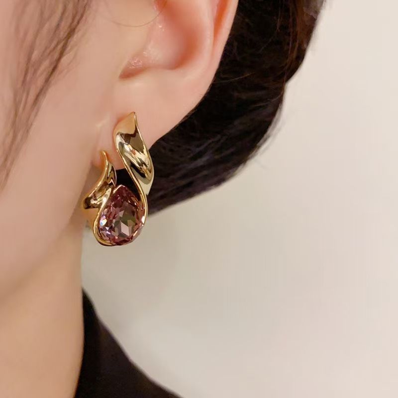 Elegant gold-plated teardrop stud earrings with pink crystal accents, displayed on a soft background.
