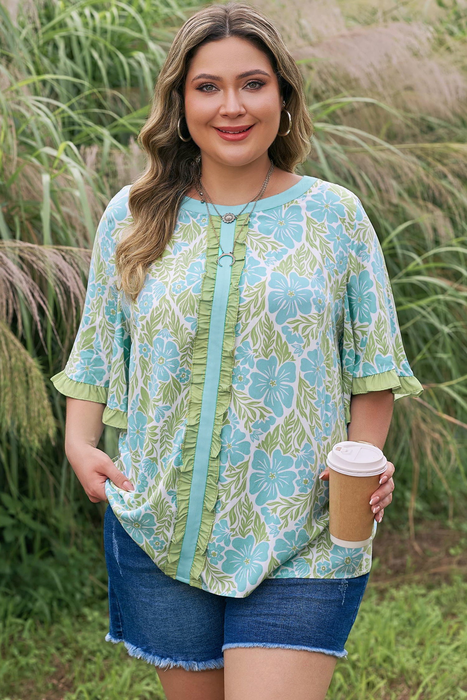 Woman wearing Elina floral short sleeve blouse with ruffled sleeves and color block trim in sage green and light blue