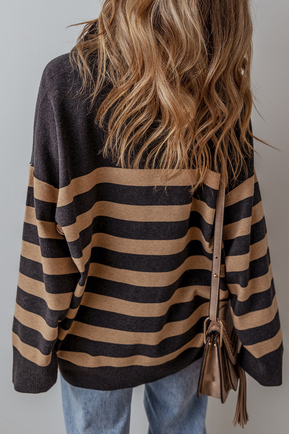 Person wearing a black and beige striped sweater with a brown leather bag on a plain background