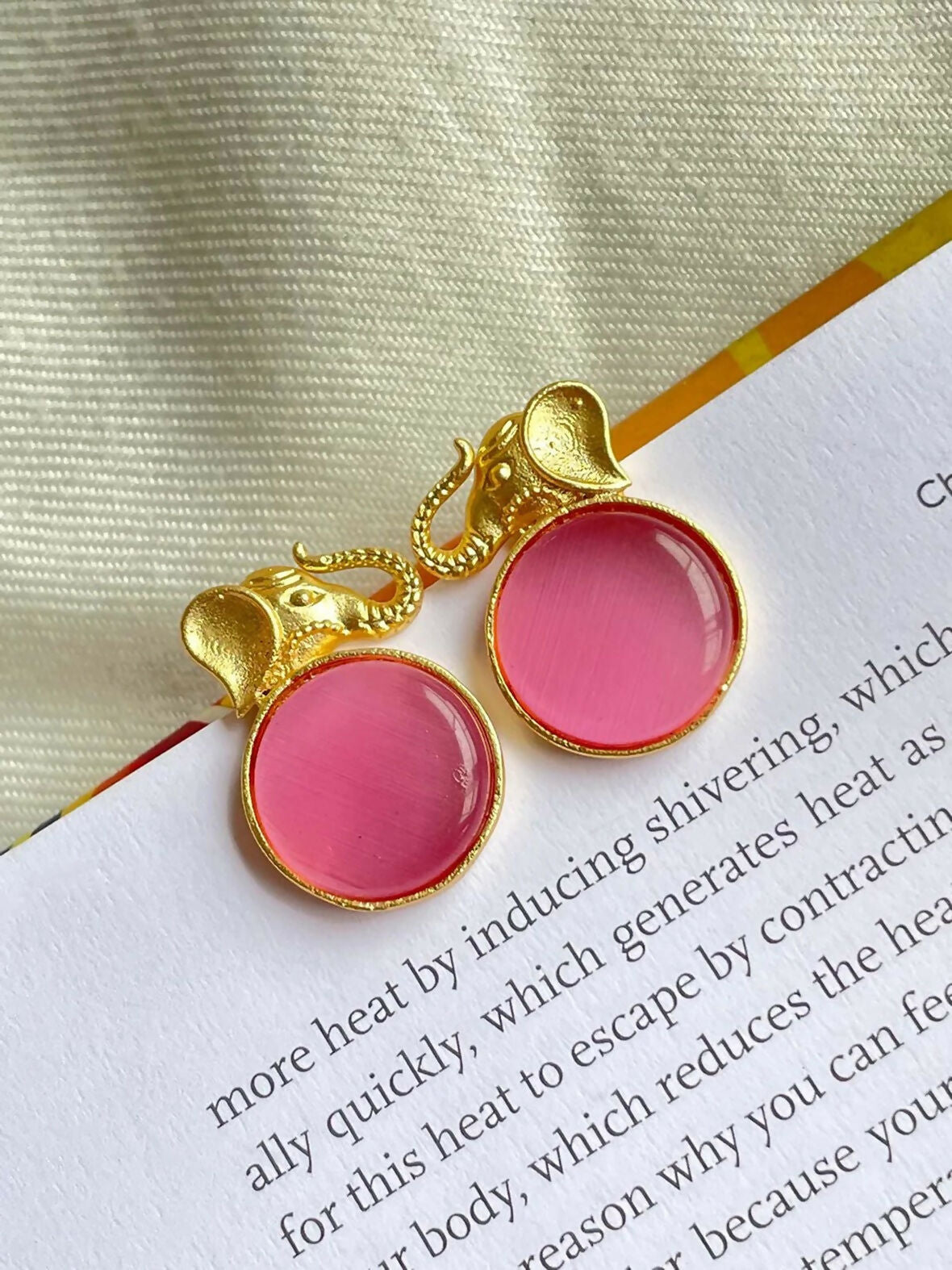 Close up of Monalisa stone elephant-shaped golden stud earrings in a peach hue.