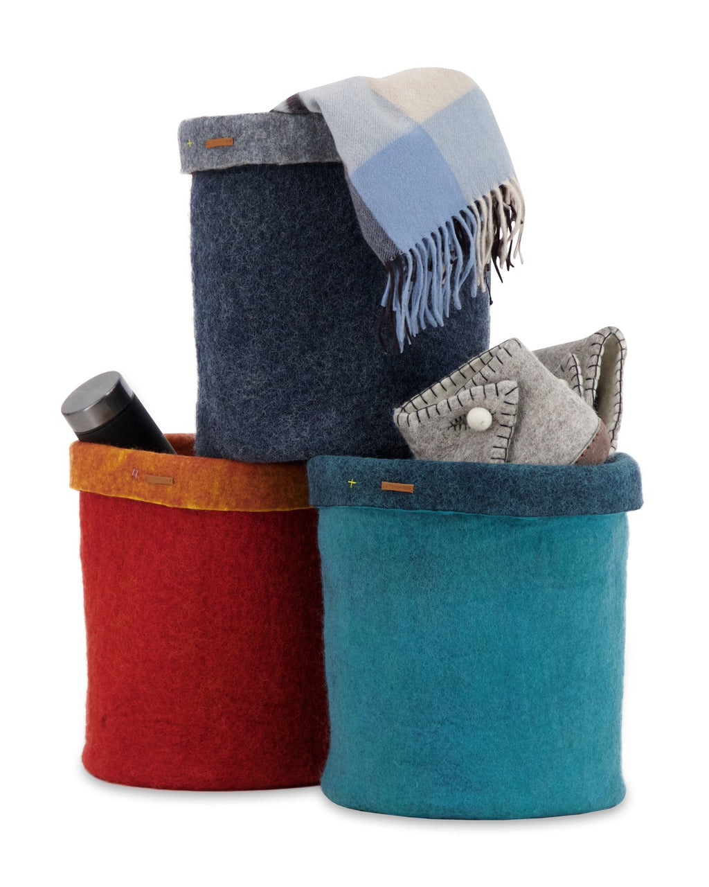 Three felt storage baskets in red, blue, and multicolor with a blanket and phone on a white background.