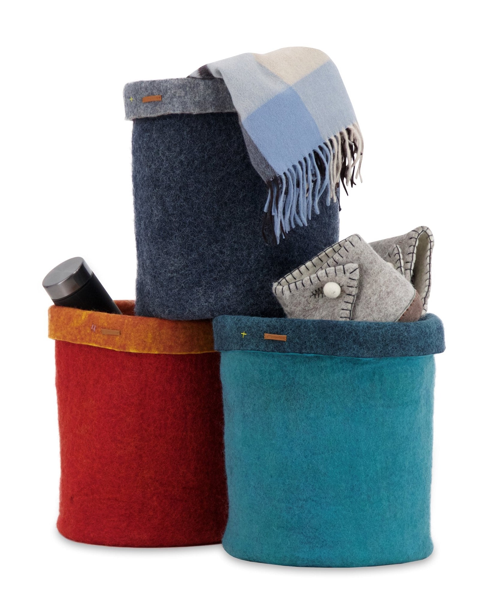 Three felt storage baskets in red, blue, and multicolor with a blanket and phone on a white background.