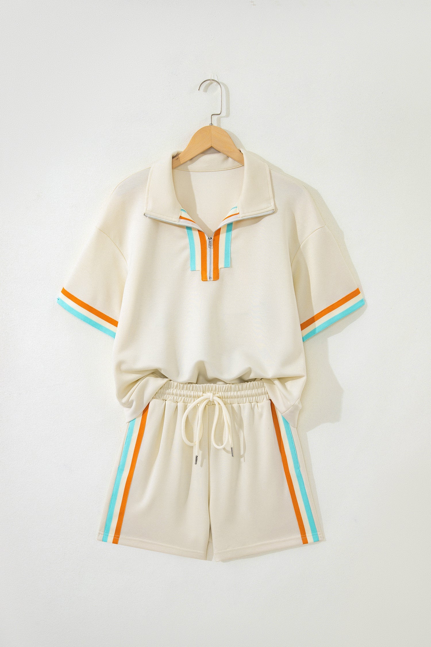 Woman wearing an off-white half-zip polo tee and matching shorts with orange and light-blue striped accents.