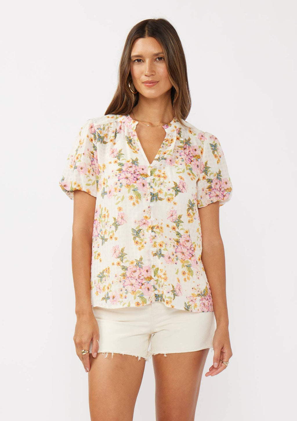 Close up of a woman wearing a natural and dusty pink floral print button-down top with short puff sleeves.