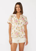 Close up of a woman wearing a natural and dusty pink floral print button-down top with short puff sleeves.