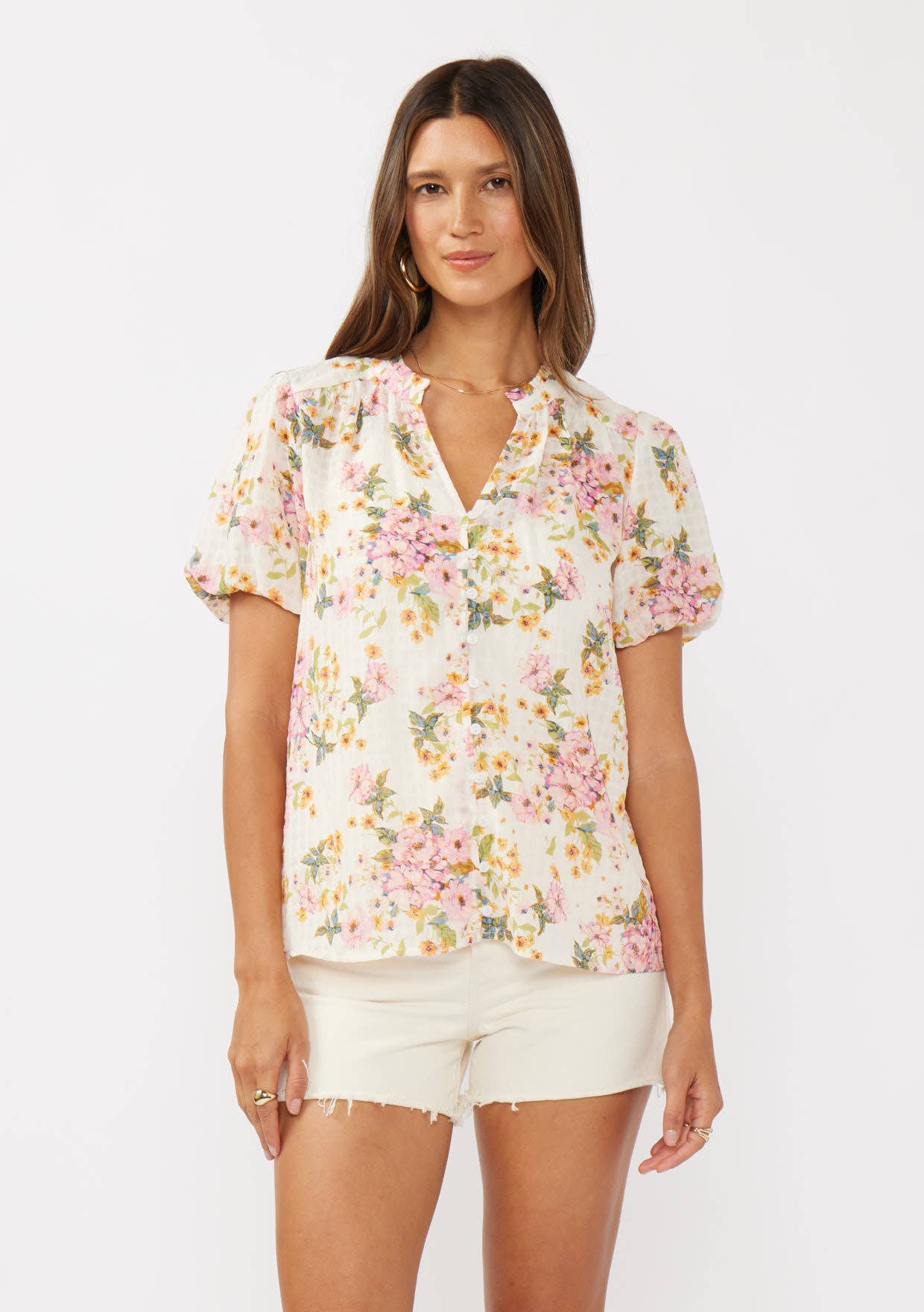 Close up of a woman wearing a natural and dusty pink floral print button-down top with short puff sleeves.