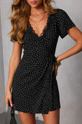 Model wearing a black and white polka dot mini dress with lace trim and v-neck wrap closure