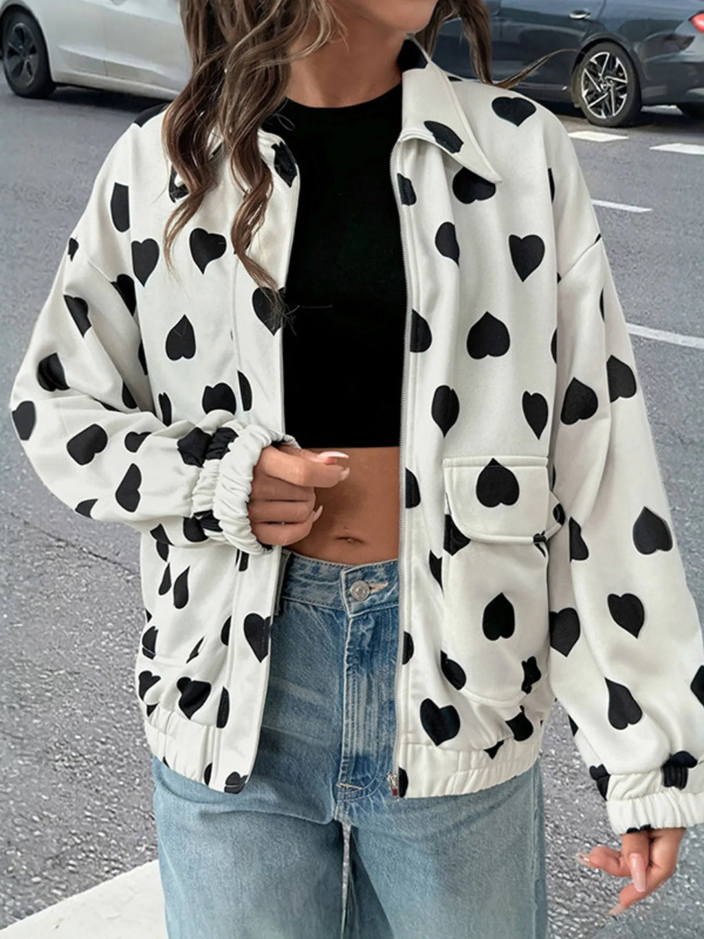 Model wearing a white zip-up jacket with black heart print featuring front pockets and elastic cuffs