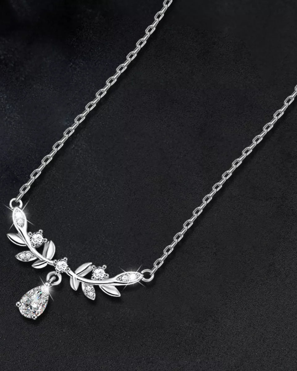 Silver necklace with leaf and teardrop pendant on a dark background