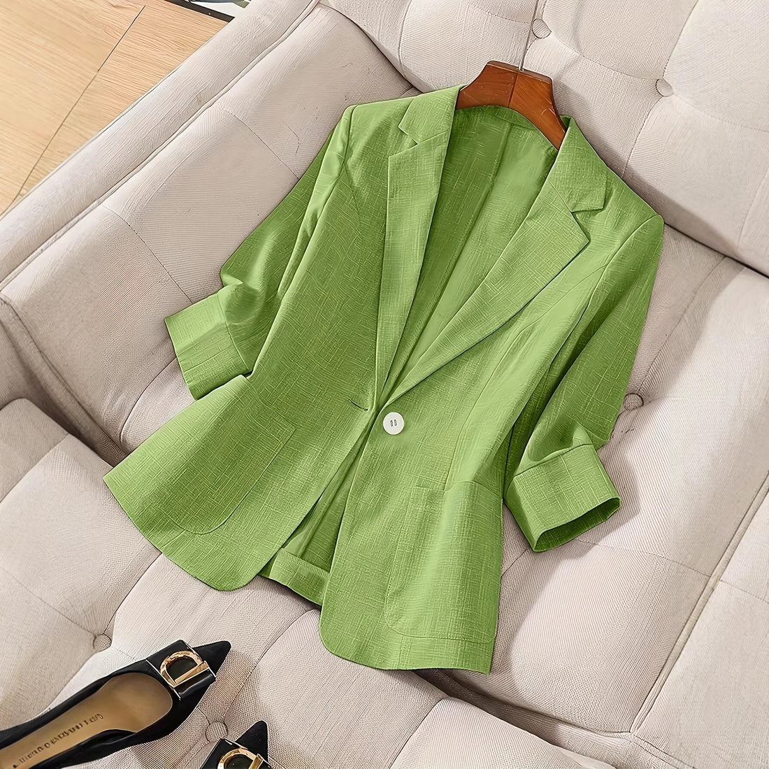A light green three-quarter sleeve single-button casual blazer displayed flat on a textured cushion.