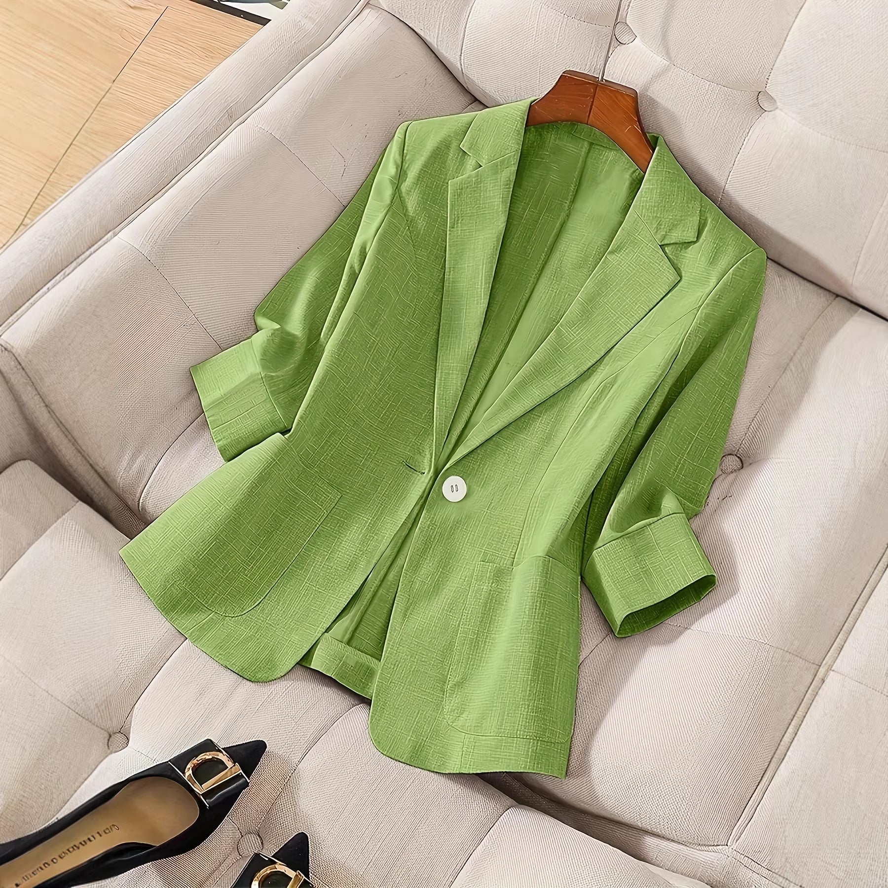 A light green three-quarter sleeve single-button casual blazer displayed flat on a textured cushion.