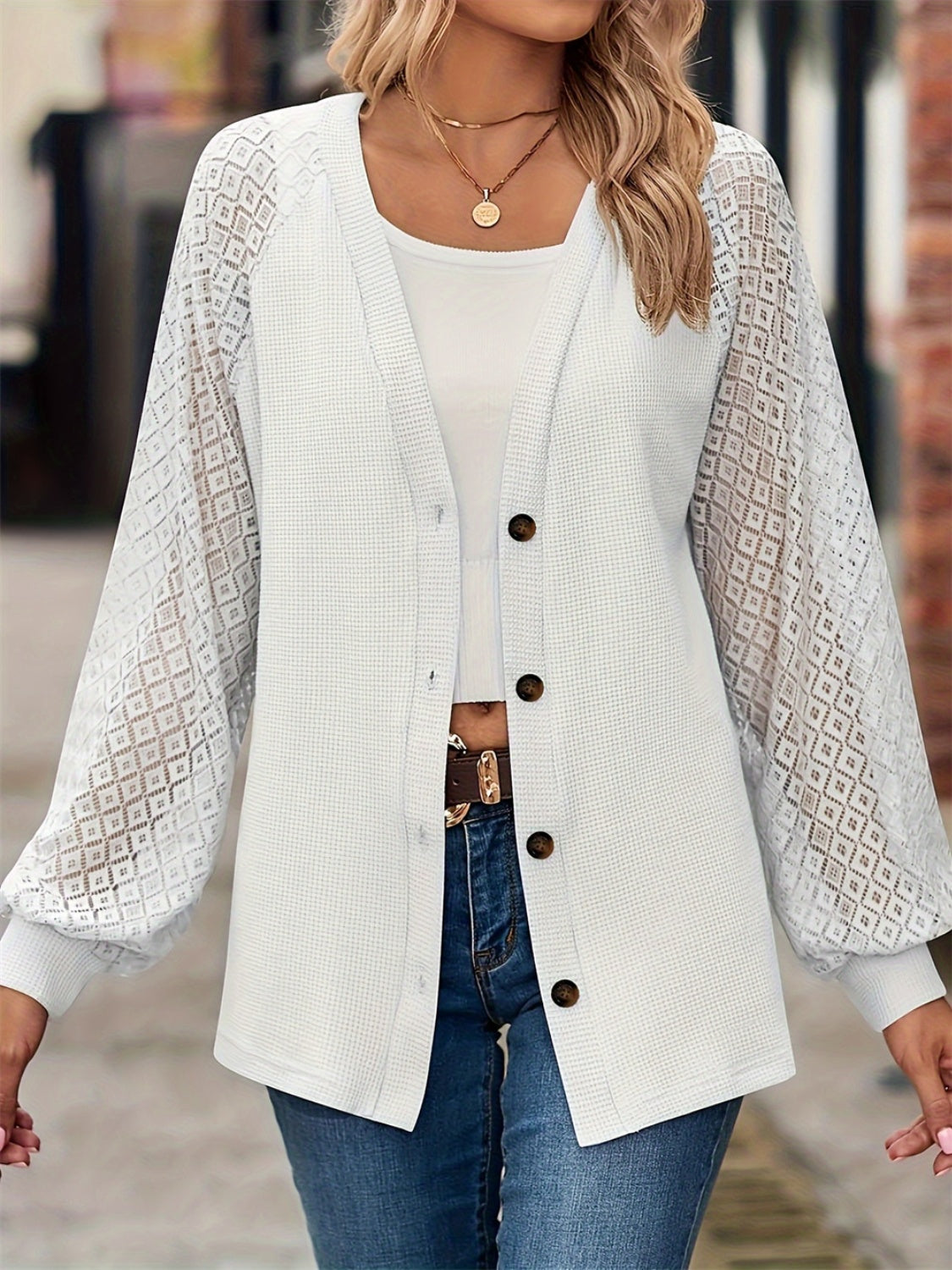 A woman wearing a white button-up V-neck cardigan with intricate lace long sleeves.