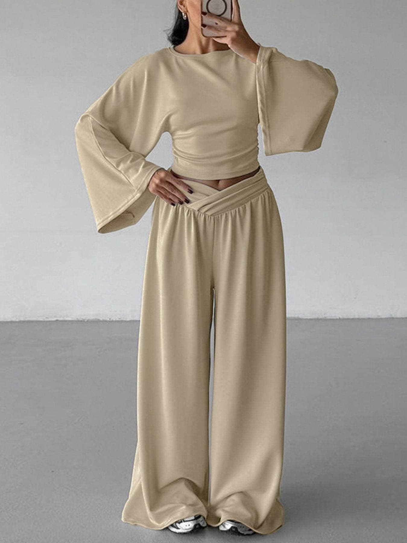 Person wearing a beige outfit with wide sleeves and high-waisted pants against a plain background