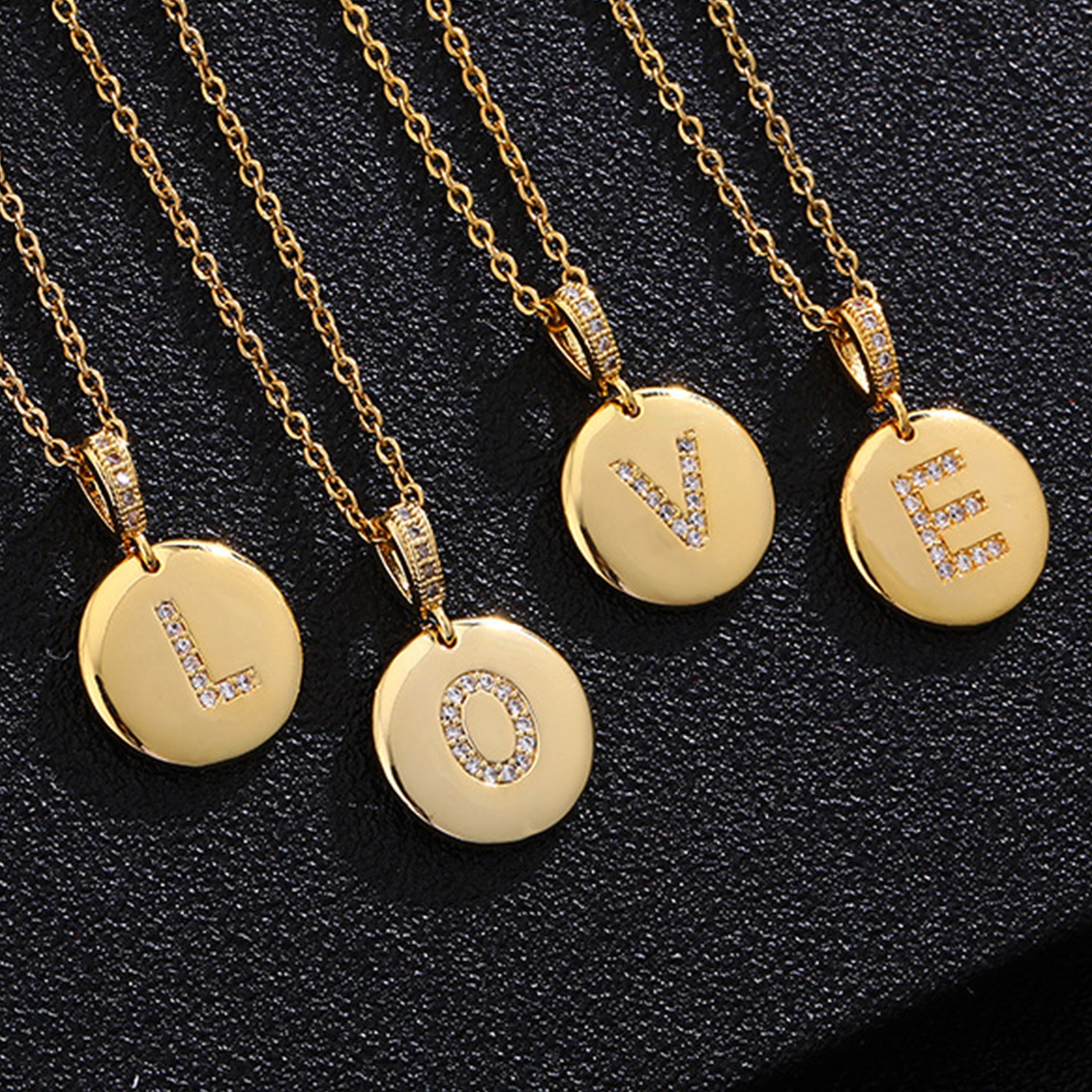 A close-up of a gold-plated initial disc necklace featuring a sparkling zircon letter pendant.