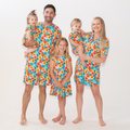 A woman wearing a vibrant tropical floral print short pajama set with a button-down top and matching elastic waist shorts.