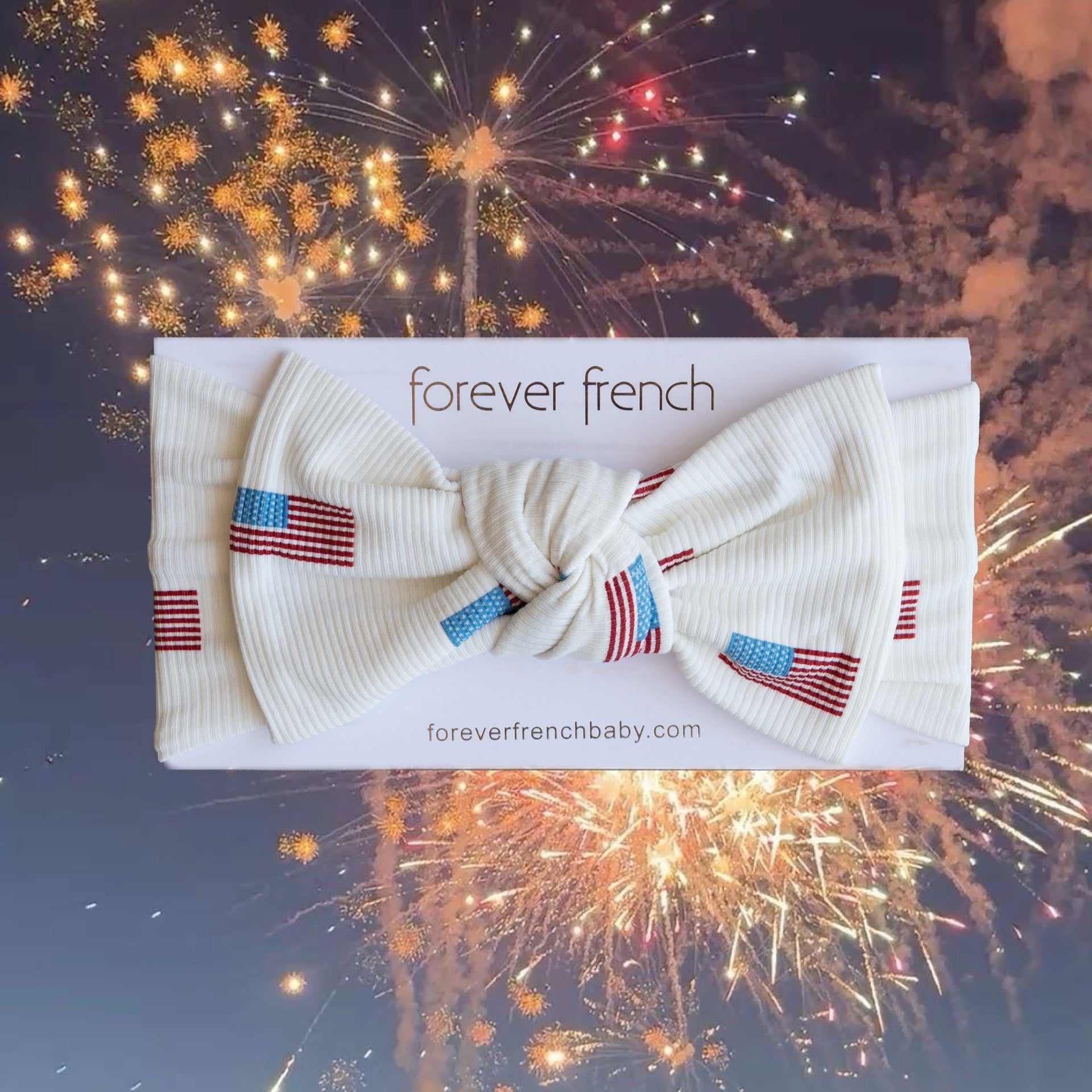 Baby wearing an Americana print bamboo head wrap with a bow, patriotic red, white, and blue theme.