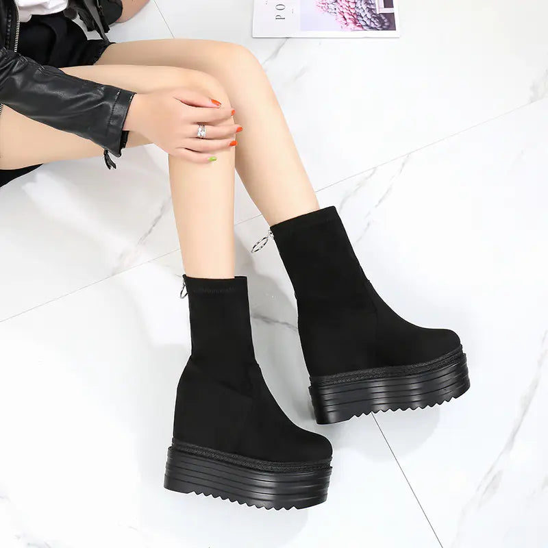 Close up view of women wearing black platform Martin boots with high heels on a white marble background.
