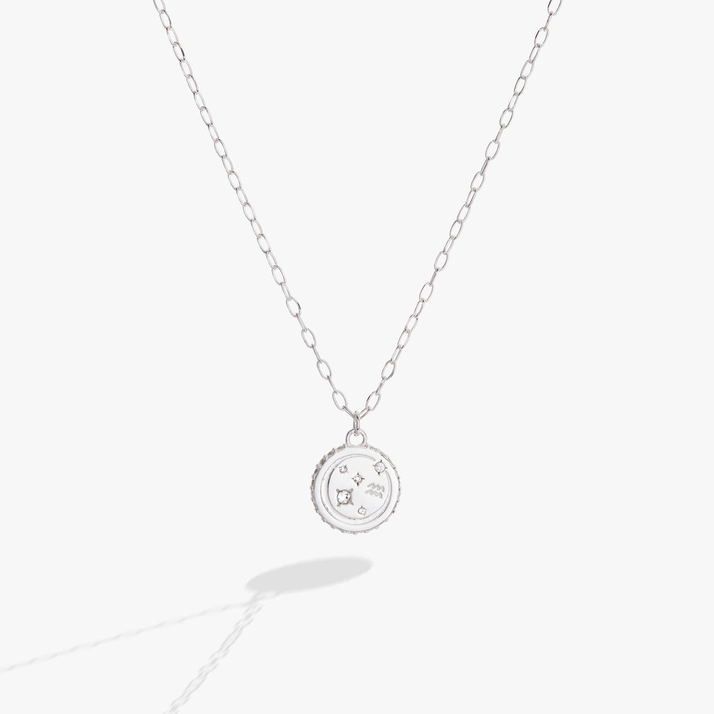 Close up of an Aquarius zodiac necklace featuring a double-sided engraved charm with crystal accents.