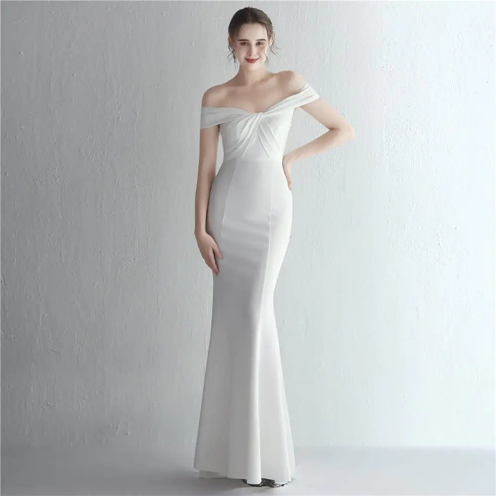 A woman wearing a slim-fit, floor-length off-shoulder gown available in multiple solid colors.