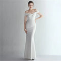 A woman wearing a slim-fit, floor-length off-shoulder gown available in multiple solid colors.
