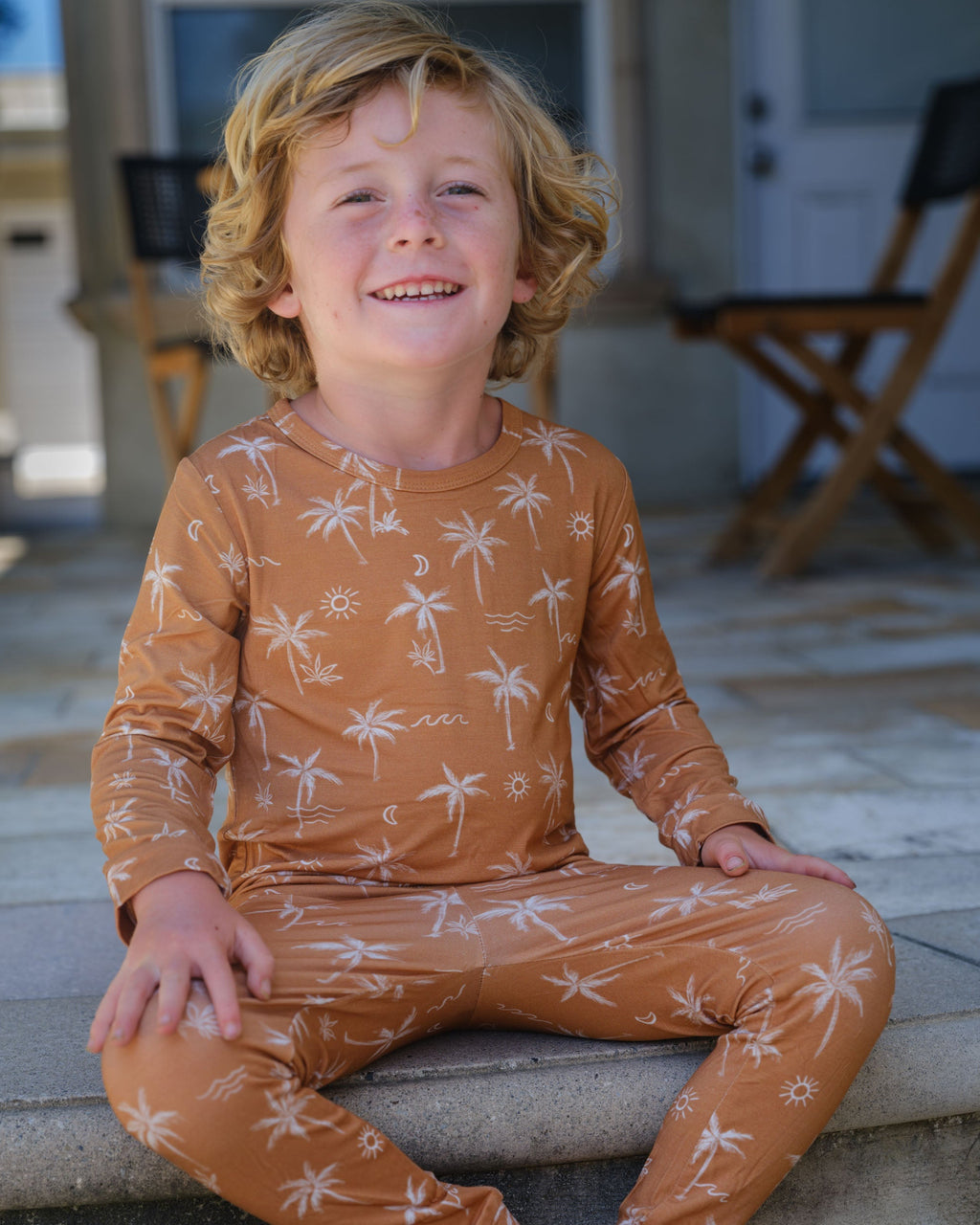 Child wearing a brown pajama set with palm tree pattern sitting on a stone step.