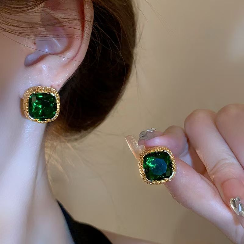 Elegant emerald stud earrings with high-quality silver posts on a display background
