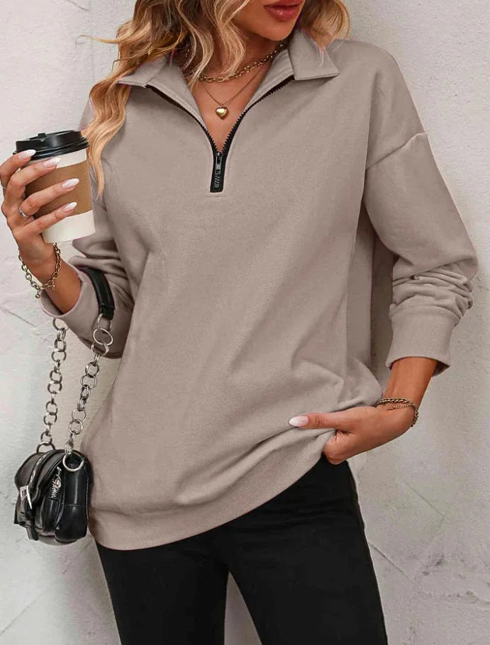 Woman wearing a beige long-sleeve top with a zipper, holding a coffee cup and a black handbag.