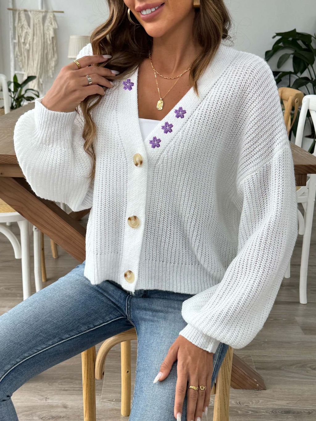 White V-neck button-up cardigan with purple floral embroidery on the shoulder and chest, modeled with jeans.