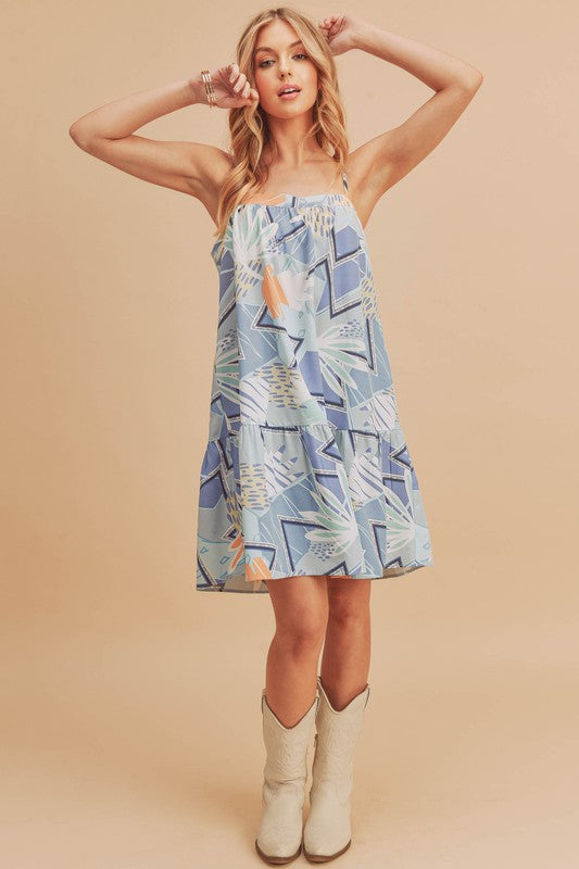 A modern square neck mini cami dress with an abstract print and ruffled hem.