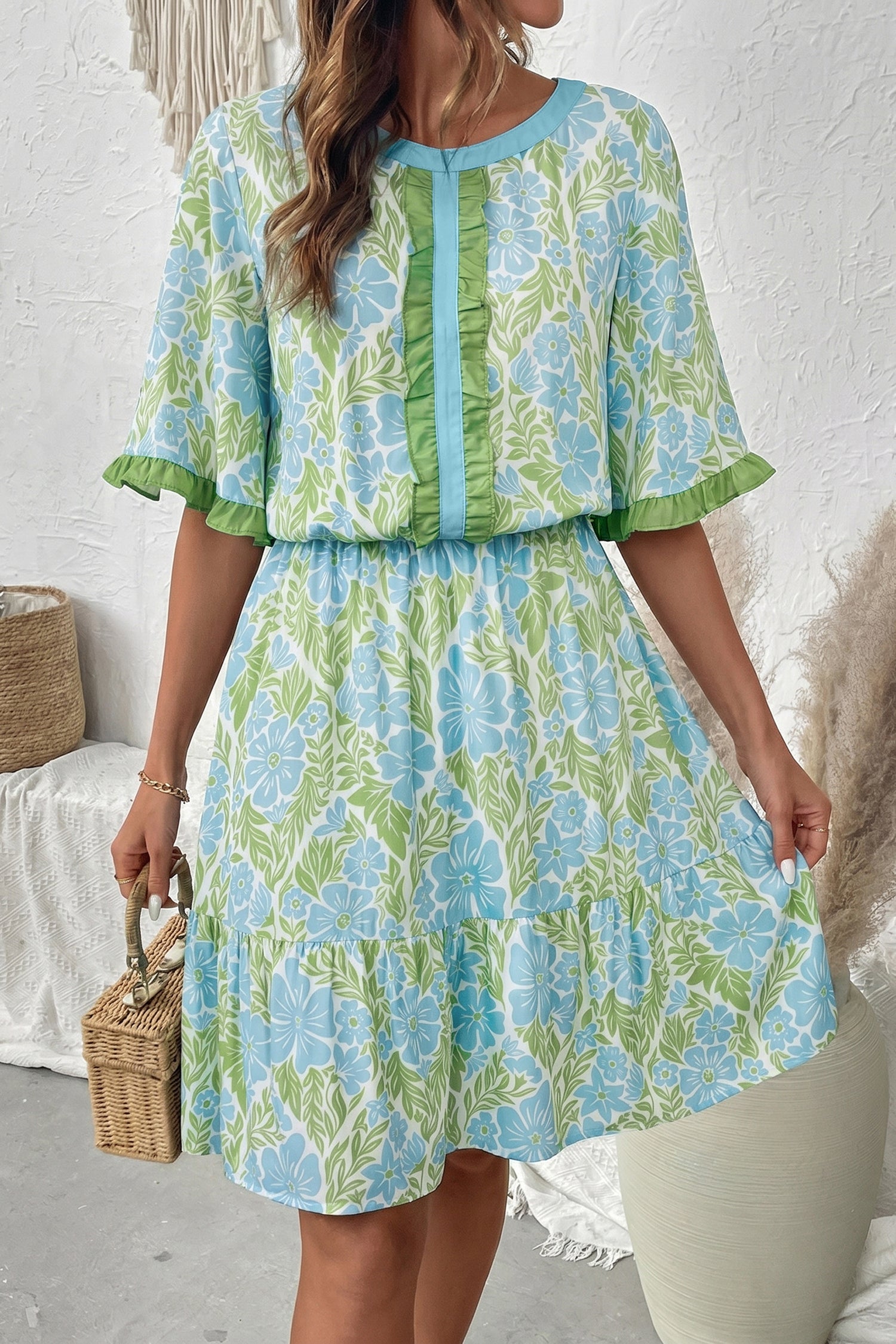 A woman wearing a bohemian-style Ophelia floral mini dress in bright blue and green with ruffled sleeves and a relaxed A-line fit.