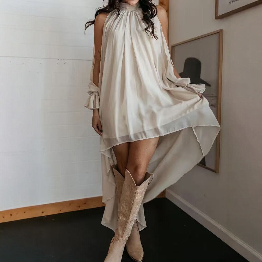 A woman wearing a beige high neck asymmetric chiffon maxi dress with long sleeves and back ribbon tie, paired with cowboy boots.