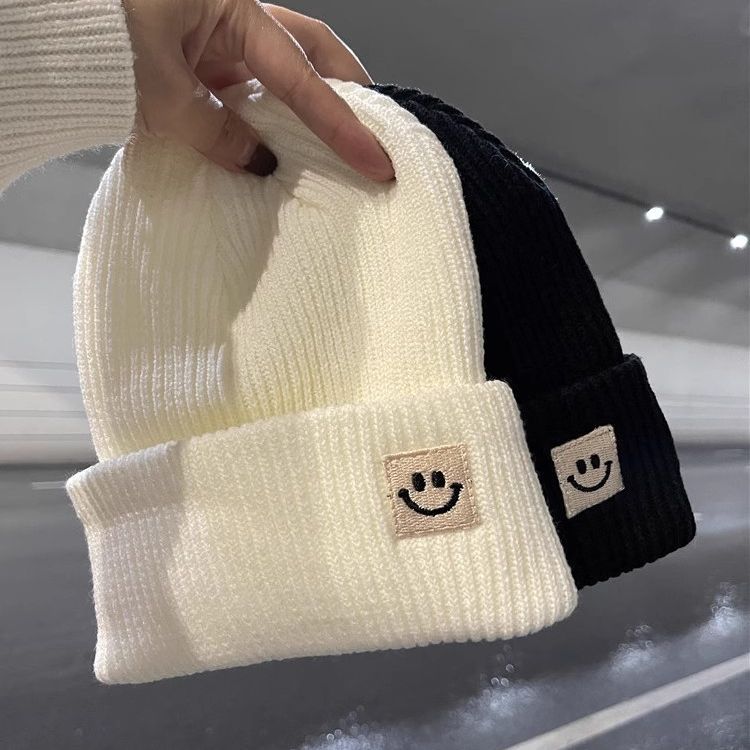Close up of various colored knitted beanies featuring a smiley face patch on the cuff