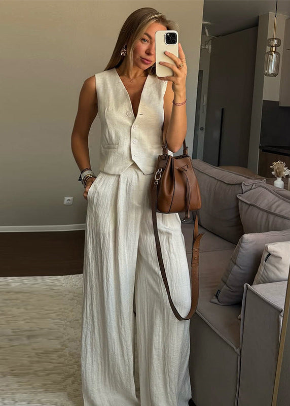 Woman taking a mirror selfie wearing a white sleeveless top and pants in a living room.