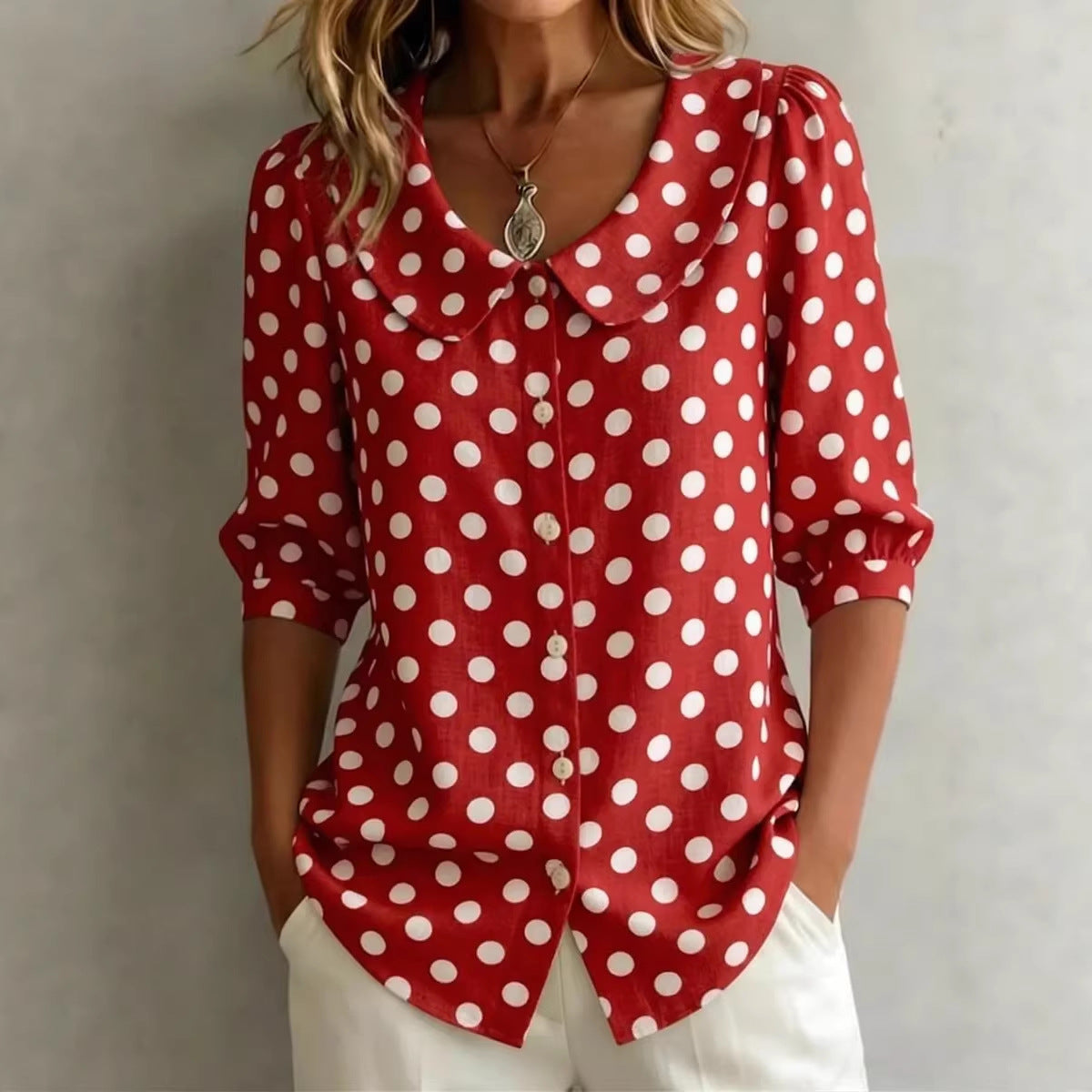 A woman wearing a red button-down shirt with a large white polka dot pattern and a peter pan collar, featuring three-quarter length sleeves.