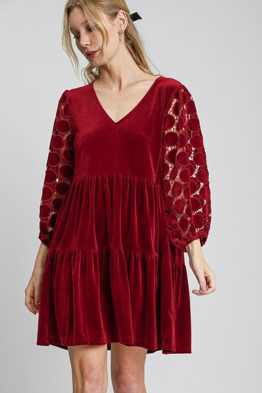 Woman wearing a burgundy velvet mini dress with tiered skirt and dotted lace sleeves