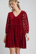 Woman wearing a burgundy velvet mini dress with tiered skirt and dotted lace sleeves