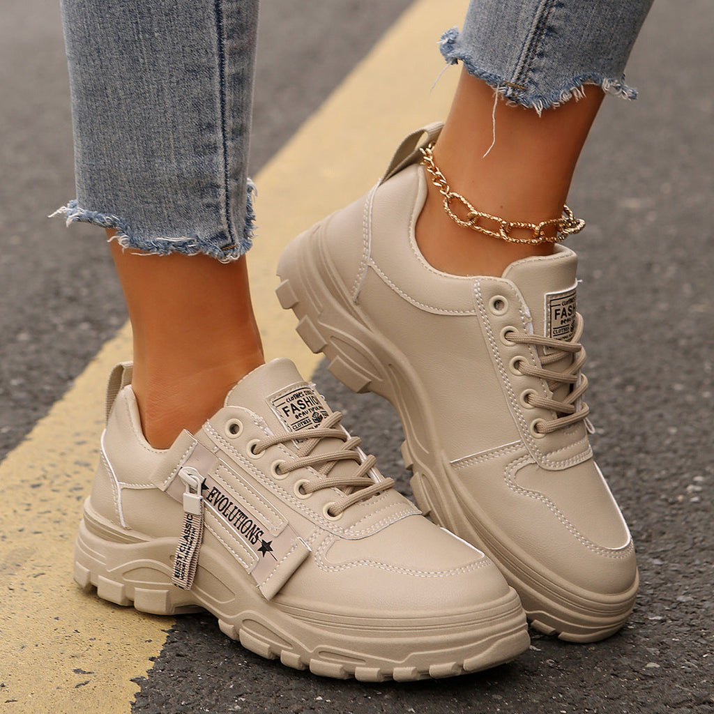 A pair of beige and black platform sneakers with side-zipper detailing, worn with jeans.