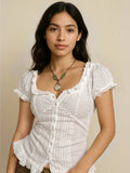 A woman wearing a white short sleeve blouse with ruffles on the collar and sleeves, featuring a button-down front and embroidered details.
